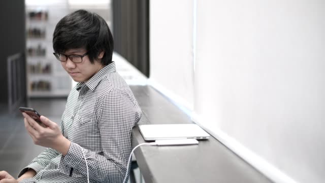 Junge-asiatische-Geschäftsmann-genießen-mit-Smartphone-auf-social-Media-Anwendung-und-spielen-in-den-Pausen-im-Büro.-Urbaner-Lifestyle-in-Working-Space-Konzept.