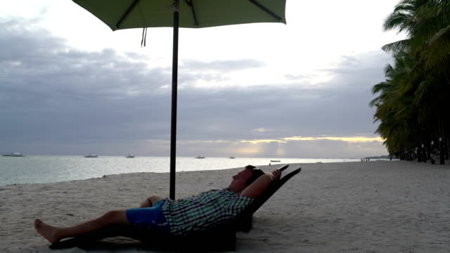 Man-resting-on-a-sun-lounger-on-the-seashore-at-sunset