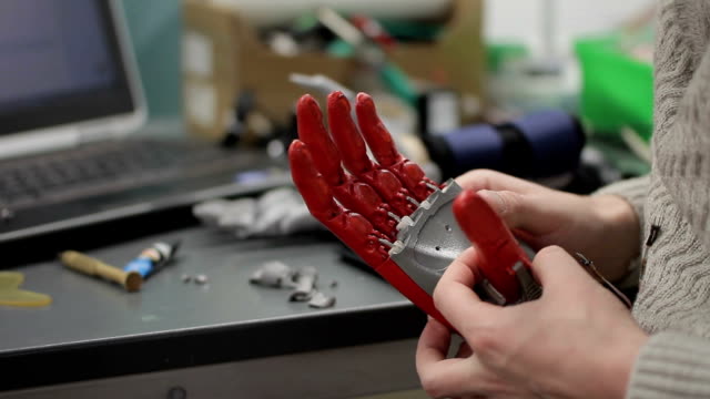 Profesionales-trabajan-con-prótesis-biónica-de-la-mano,-en-mesa-de-laboratorio-en-el-interior
