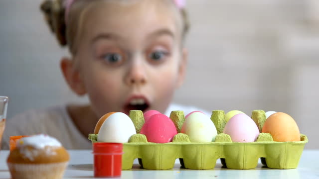 Surprised-girl-appearing-from-under-table-and-looking-at-colorful-Easter-eggs
