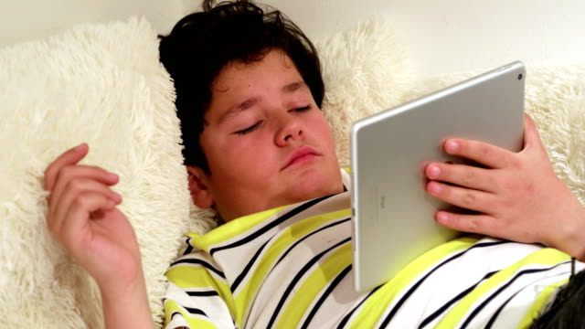 Müder-Teenager-liegend-auf-Sofa-mit-digitalem-Tablet-zu-Hause
