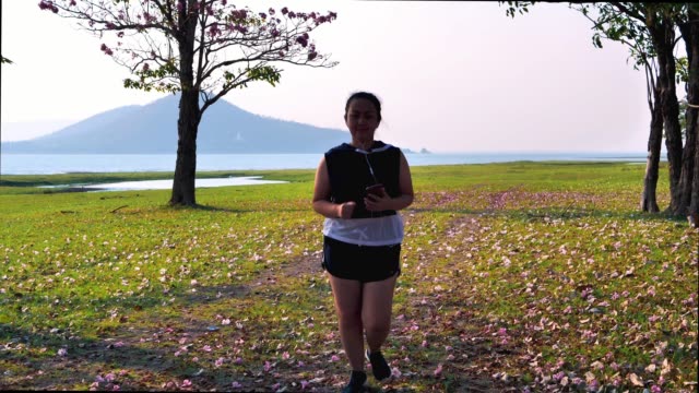 Eine-dicke-asiatische-Frau-joggt-abends-in-natürlichem-Sonnenlicht-und-hört-Musik.-Sie-versucht,-mit-Übung-Gewicht-zu-verlieren.--Konzept-Gesundheit-mit-Bewegung.