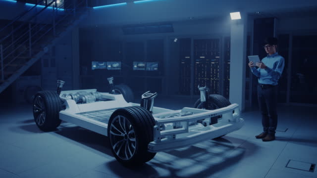 Ingeniero-de-automóviles-trabajando-en-la-plataforma-de-chasis-de-coche-eléctrico,-utilizando-Tablet-Computer-realidad-aumentada-con-modelado-de-software-CAD-3D.-Instalación-innovadora:-bastidor-del-vehículo-con-ruedas,-motor,-batería