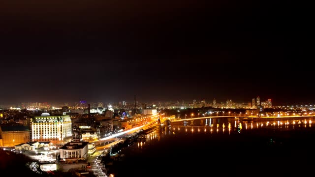 Time-lapse-video-at-night-of-big-city,-embankment-end-wide-river-with-water-waves-from-floating-boat-create-lighting-effect