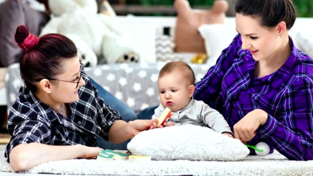 Happy-same-sex-parents-playing-with-little-cute-baby-lying-on-floor-at-home-medium-shot