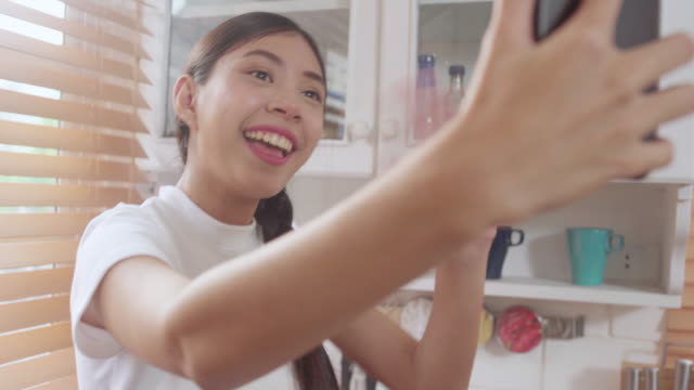 Junge-asiatische-Teenagerin-vlog-zu-Hause,-weiblich-mit-Smartphone-machen-vlog-Video-zu-sozialen-Medien-in-der-Küche.-Lifestyle-Frau-entspannen-sich-am-Morgen-bei-zu-Hause-Konzept.