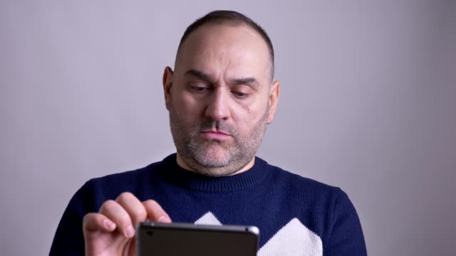 Closeup-shoot-of-middle-aged-caucasian-man-browsing-on-the-tablet-then-lookinga-at-camera-and-smiling.