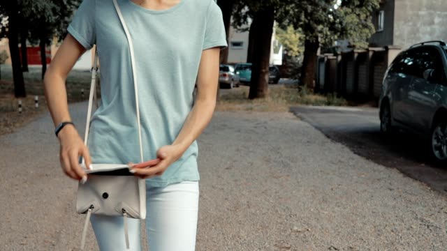 Schlanke-Mädchen-in-Jeans-und-ein-T-Shirt-nimmt-das-Telefon-aus-ihrem-Geldbeutel-und-reagieren-auf-eine-Nachricht-im-Freien