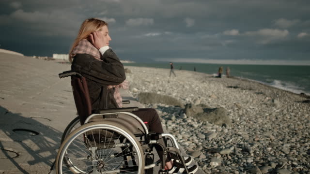 Junge-blonde-Frau-mit-Lähmung-der-Beine-sitzt-im-Rollstuhl,-Blick-auf-Meer