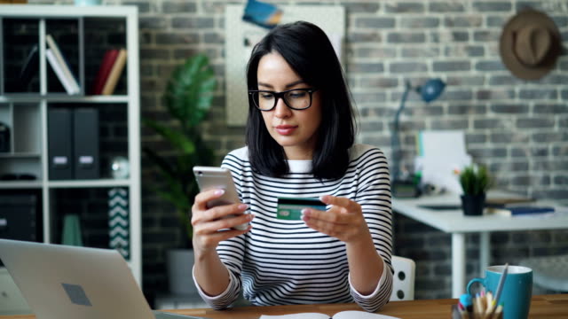 Junge-Dame-bezahlt-online-mit-Kreditkarte-mit-Smartphone-am-Arbeitsplatz