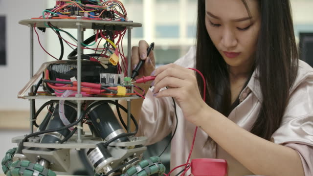La-ingeniera-de-electrónica-asiática-trabaja-con-robots,-construyendo,-arreglando-robótica-en-taller.-Personas-con-concepto-de-tecnología-o-innovación.