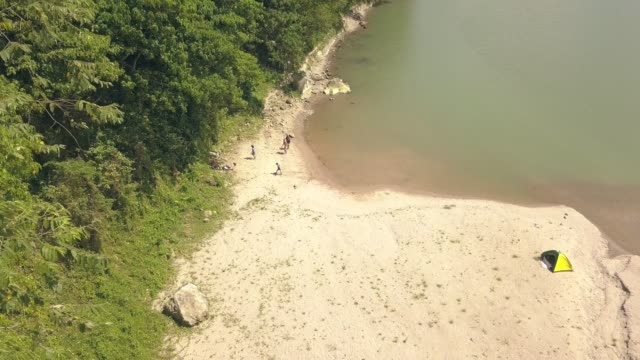 Aerial-view-tourist-people-on-camping-at-river-shore-while-summer-vacation.-Tourist-tent-on-campsite-on-lake-shore-while-summer-hike.-Tourism-and-travel-concept