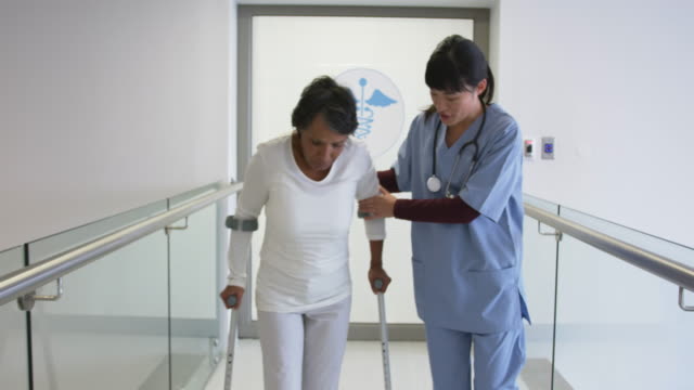 Young-doctor-helping-patient-use-crutches-in-hospital-4k