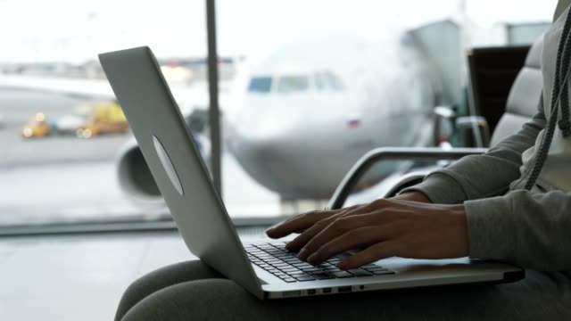 Nahaufnahme-Hände-der-Frau-arbeiten-auf-Laptop-in-Flughafenhalle-Hintergrund-des-Flugzeugs-im-Fenster-wartet-auf-Boarding