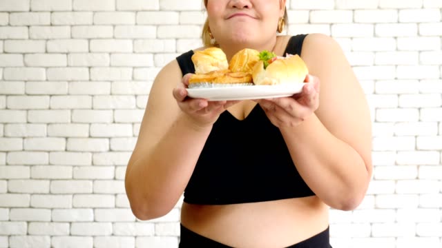 Übergewichtige-junge-Frau-in-Sportbekleidung-halten-Hot-Dog-und-Brötchen