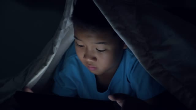 Kleiner-Junge-mit-Tablet-te-unter-Decke-in-der-Nacht-im-Bett.