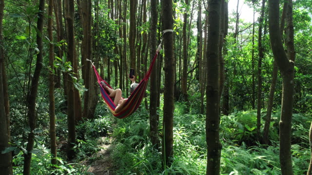 Aerial-view-of-relaxing-in-hammock-taking-selfie-with-smart-phone-in-tropical-rainforest