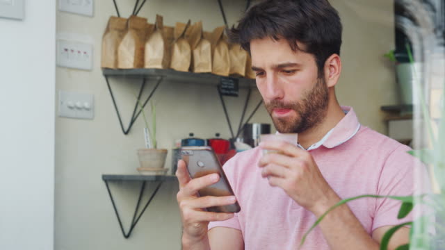 Junger-Mann-in-Coffee-Shop-Blick-auf-Handy