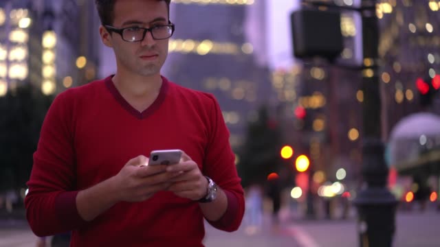 Millennial-spanischen-Hipster-Kerl-in-Brille-tippen-Textnachricht-auf-Webseite-beim-Bummeln-in-der-Innenstadt