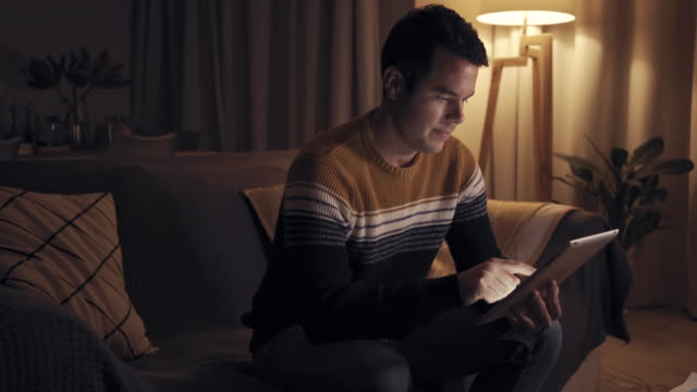 Junger-Mann-in-der-späten-Nacht-sitzen-auf-der-Couch-tippen-auf-digitalen-Tablet-im-modernen-Wohnzimmer-spät-in-der-Nacht