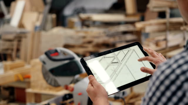 Close-up-of-woodworker-using-tablet-at-work-looking-at-furniture-design