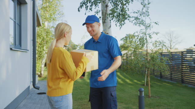 Beautiful-Young-Woman-Meets-Delivery-Man-who-Gives-Her-Cardboard-Box-Package,-She-Signs-Electronic-Signature-POD-Device.-Courier-Delivering-Parcel-in-the-Suburban-Neighborhood.-Side-View
