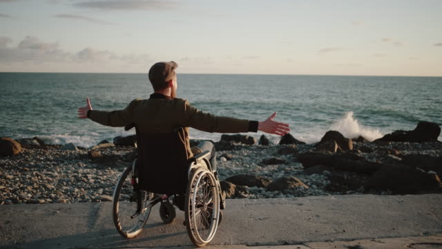 Hombre-discapacitado-está-observando-el-horizonte-marino-y-levantando-la-mano-hacia-arriba,-vista-trasera