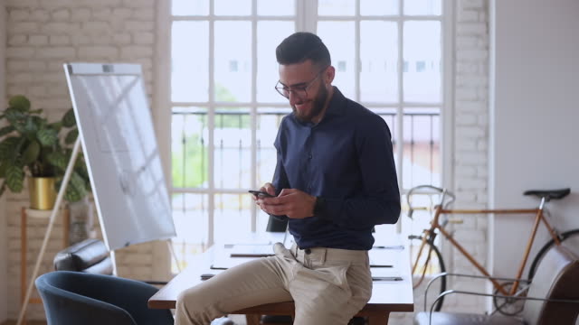 Smiling-young-entrepreneur-using-smartphone-mobile-apps-in-modern-office