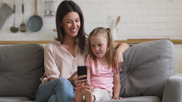 Glückliche-Mutter-und-Kind-Tochter-genießen-mit-Smartphone-auf-dem-Sofa