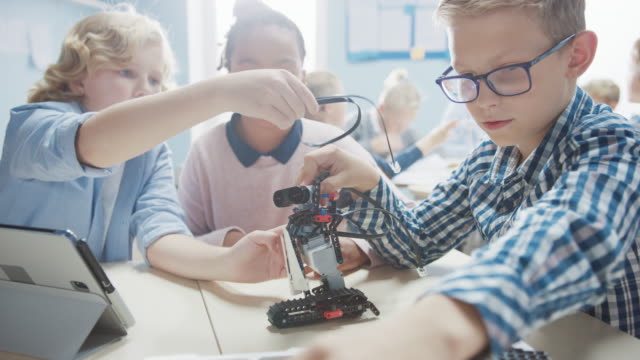 Aula-de-Robótica-de-la-Escuela-Primaria:-Grupo-Diverso-de-Niños-Construyendo-y-Programando-Robots-Juntos,-Hablando-y-Trabajando-en-Equipo.-Diseño-de-software-de-aprendizaje-para-niños-e-ingeniería-de-robótica-creativa