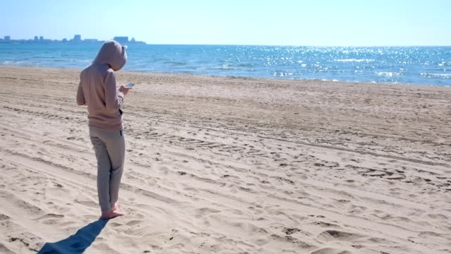 Unrecognizable-woman-is-typing-on-phone-on-the-beach-by-sea.