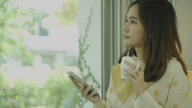 Close-up-shot-of-4K-footage-of-young-asian-woman-using-mobile-and-drinking-coffee-near-the-window-in-the-morning.