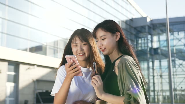 Close-view-of-happy-lovely-young-asian-girls-in-fashion-clothes-standing-in-front-of-airport-and-looking-at-the-phone