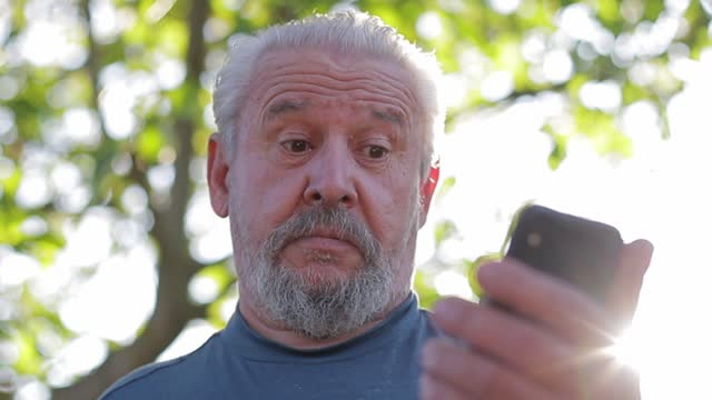 Alter-grauhaariger-Mann-mit-Bart-benutzt-ein-modernes-Smartphone