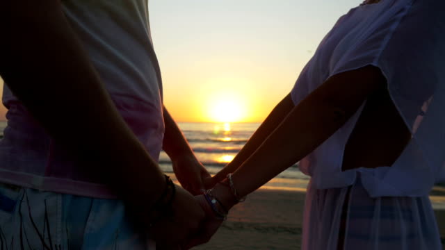 Romantisches-Paar-Hand-in-Hand-und-Wandern-am-Strand-in-Richtung-Meer