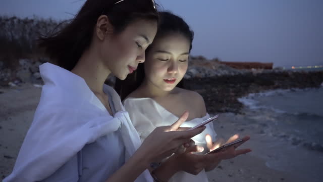 Zwei-Frauen-stehen-spielen-das-Telefon-in-der-Nacht.-Technologiekonzepte-können-überall-kommunizieren.