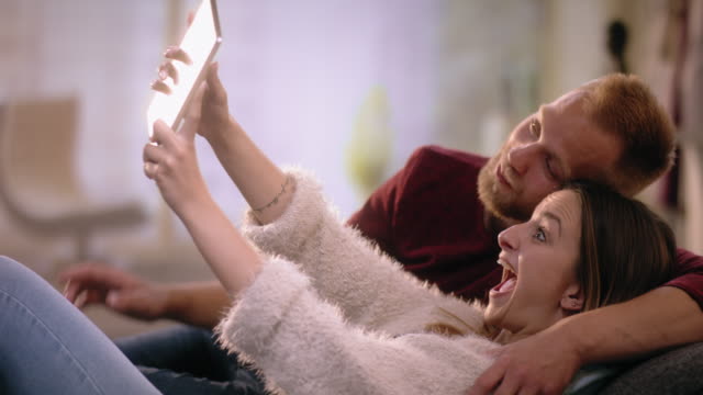 Young-oouple-in-love-on-sofa-home-making-a-selfie-with-tablet
