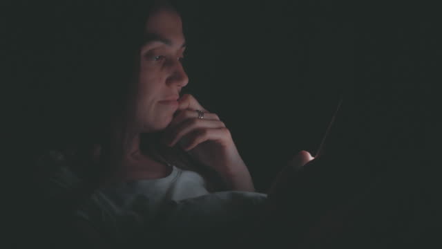 Young-woman-using-cellphone-on-bed-at-night