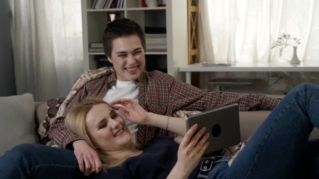 Lesbisches-Paar-ruht-auf-der-Couch,-mit-Tablett-und-lachen,-junge-Familie,-Plaid,-gemütliche-60-fps