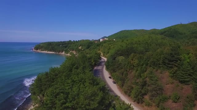 Video-from-the-drone-flying-along-the-coast.-A-road-passes-along-the-shore.-Montains-and-foresst-on-the-ocean-coast