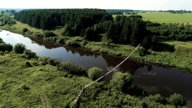 Flying-over-the-village,-fields,-river-and-forests.-Beautiful-bird's-eye-view-on-hanging-old-bridge-over-the-river.