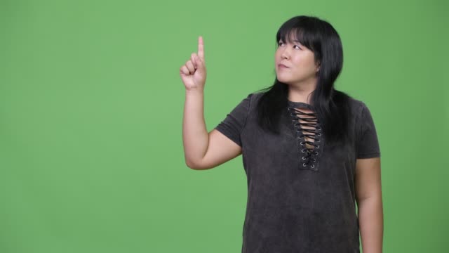 Mujer-asiática-con-sobrepeso-feliz-pensando-mientras-el-dedo-acusador