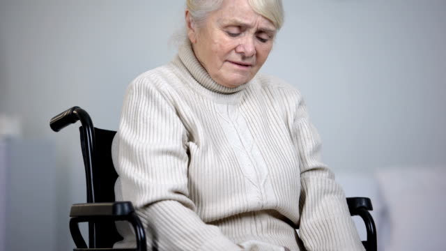 Elderly-woman-in-wheelchair-massaging-painful-knee-joints,-health-problems