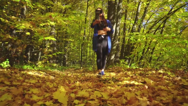 Blogger-charismatische-junge-Frau-ist-im-herbstlichen-Wald-spazieren-und-Videoaufnahme-für-Vlog-mit-Kamera-sprechen-aktiv-gestikulieren-und-lächelnd