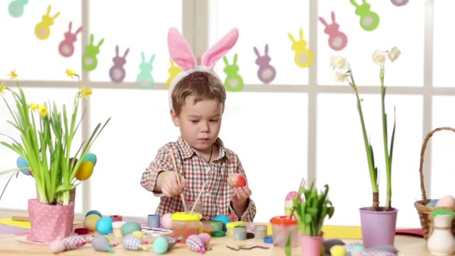 Glückliches-Kind,-das-am-Ostersamstag-hanagende-Hosen-trägt,-die-Eier-malen.