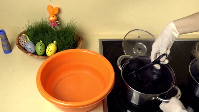 Hände-nehmen-bemalte-Eier-aus-Topfwasser-mit-Farbe-zu-Kunststoffschale-mit-Wasser