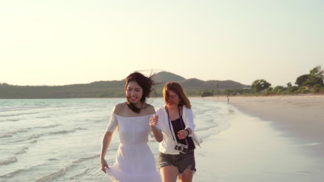 Junges-asiatisches-lesbisches-Paar-läuft-am-Strand.-Schöne-Freundinnen-freuen-sich,-sich-bei-Sonnenuntergang-am-Abend-am-Strand-am-Meer-zu-vergnügen.-Lifestyle-lesbisches-Ehepaar-reist-nach-Strandkonzept