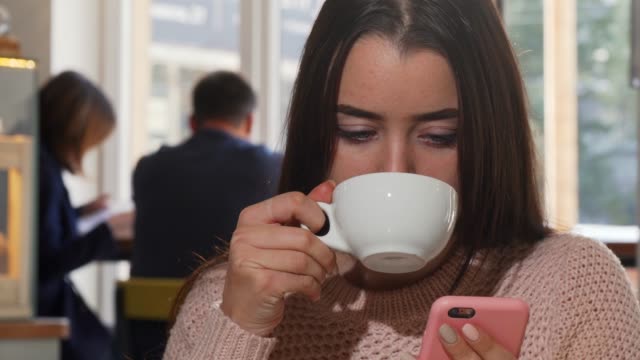 Atractiva-mujer-bebiendo-café,-usando-su-teléfono-inteligente-en-el-café