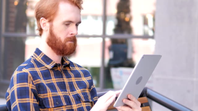 Bart-junge-Mann-mit-Tablet-beim-Sitzen-im-Freien