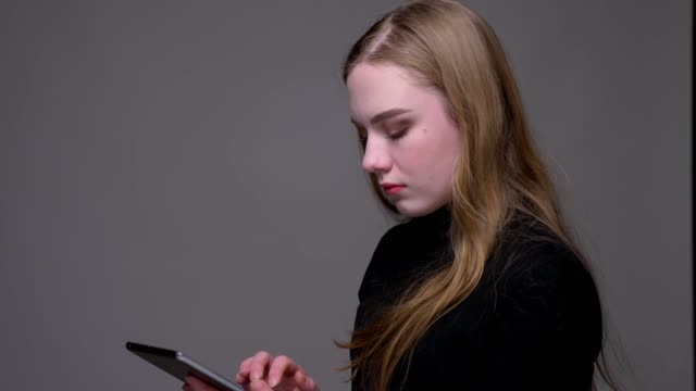Nahaufnahme-Porträt-von-jungen-attraktiven-Brünette-weiblich-Browsing-auf-dem-Tablet-mit-Hintergrund-isoliert-auf-grau